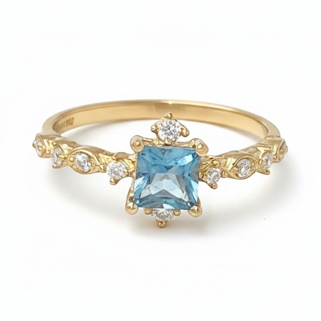 Jade18k yellow gold ring featuring a square-cut blue gemstone center with sparkling accent stones and intricate band detailing.