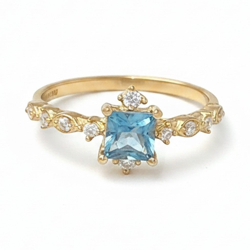 Jade18k yellow gold ring with a square-cut blue gemstone center and sparkling accent stones on a detailed band.