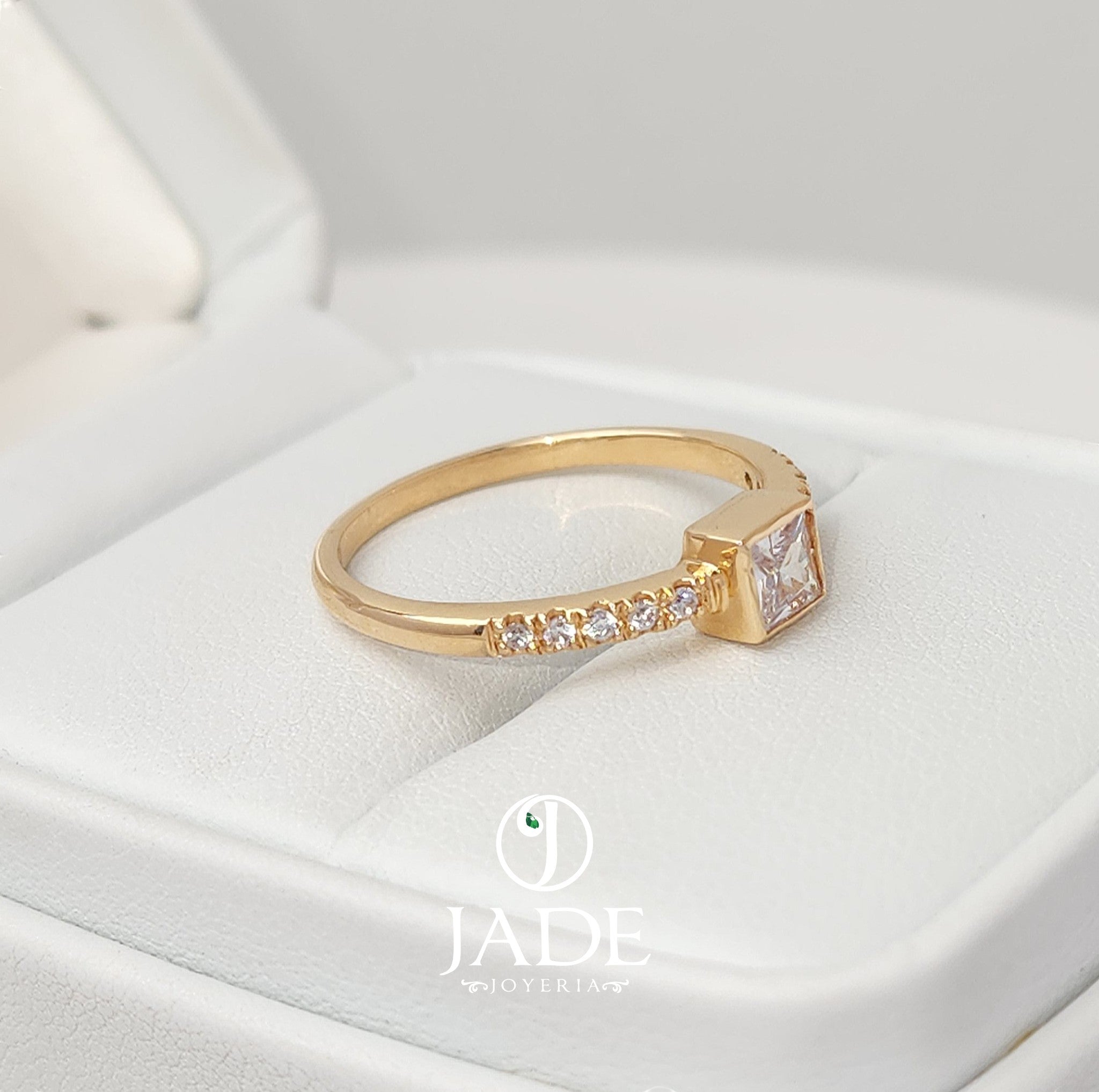 Jade18k Laura engagement ring in 18k orange gold with a princess-cut cubic zirconia and small stones on the band.