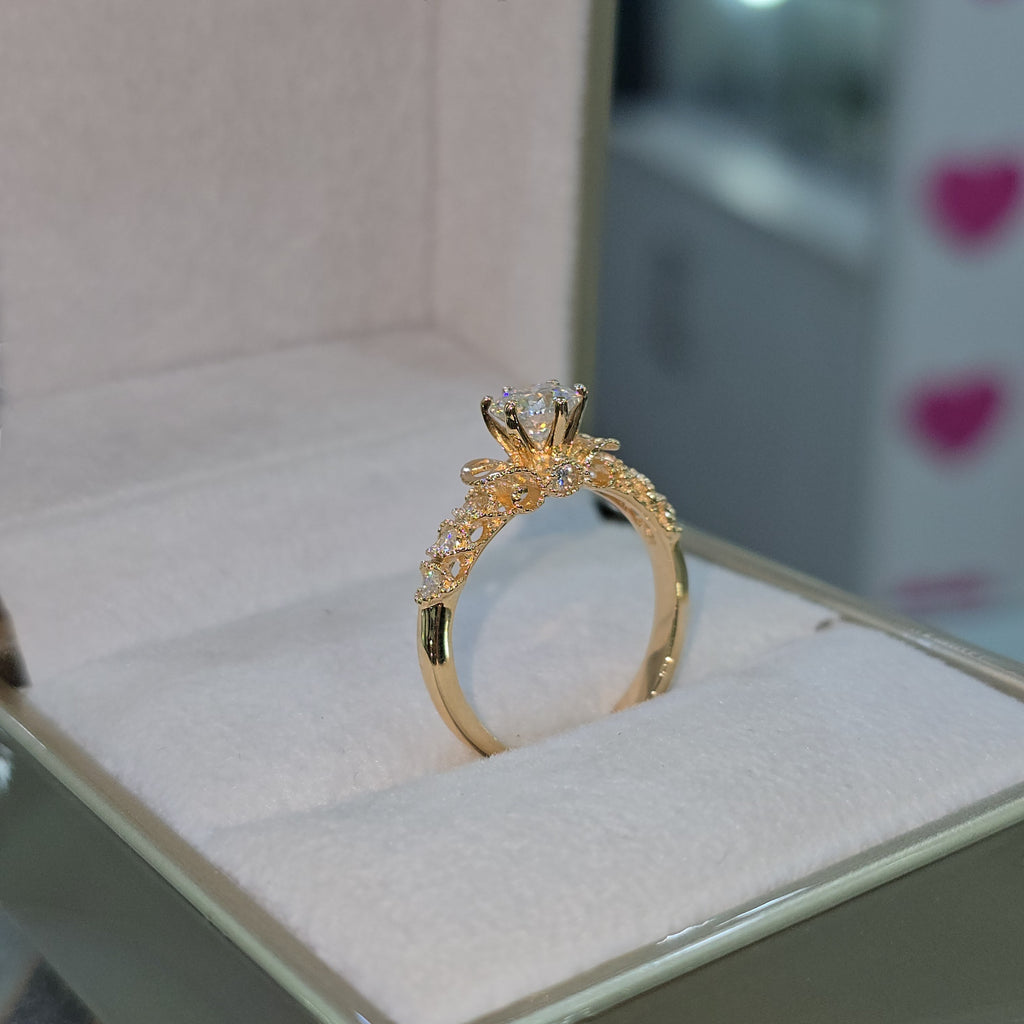 Jade18k engagement ring with moissanite center stone and intricate 18K orange gold band with small diamonds.