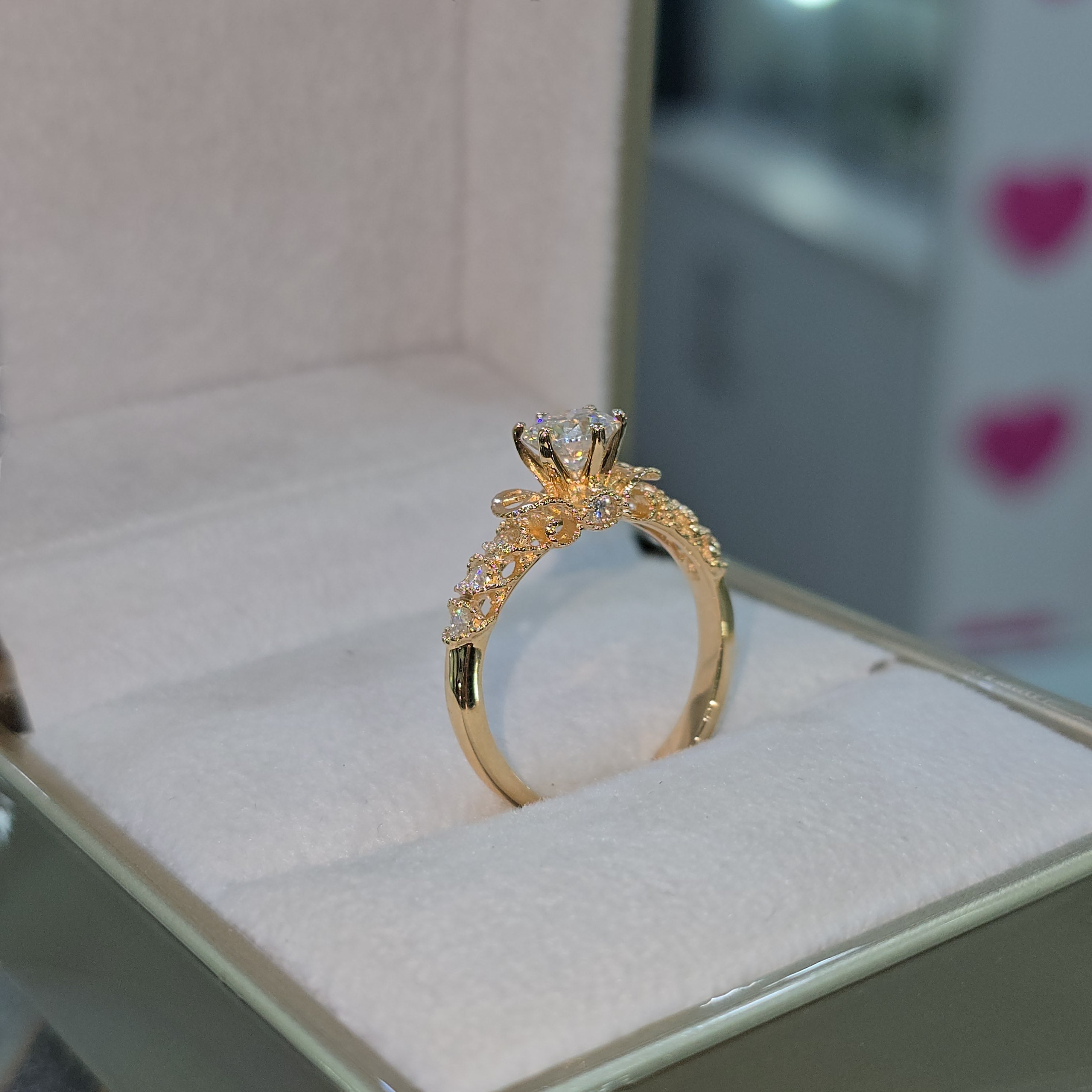 Jade18k engagement ring with moissanite center stone and intricate 18K orange gold band with small diamonds.