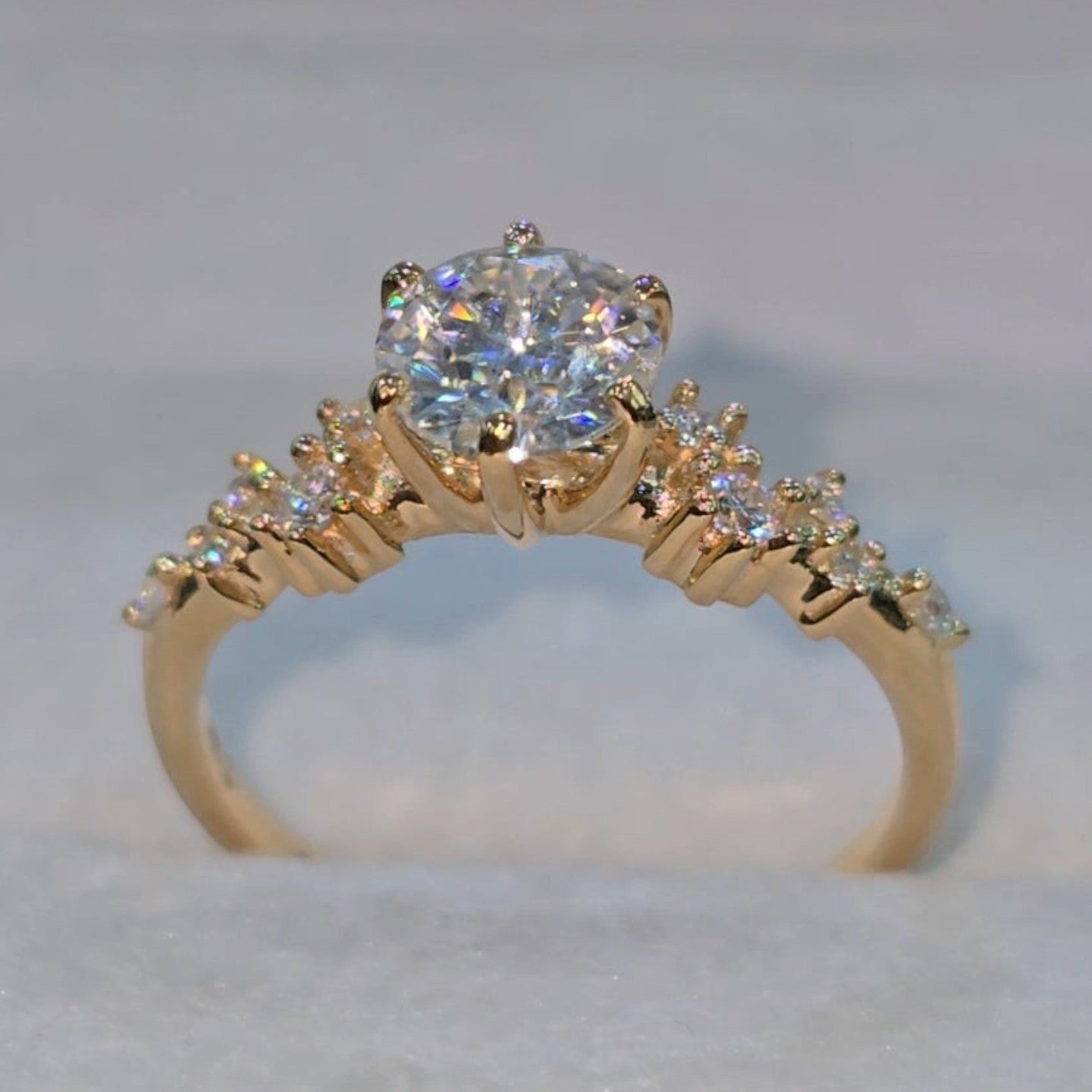 Jade18k engagement ring with a large round moissanite center stone and smaller stones on the band, set in 18k orange gold.
