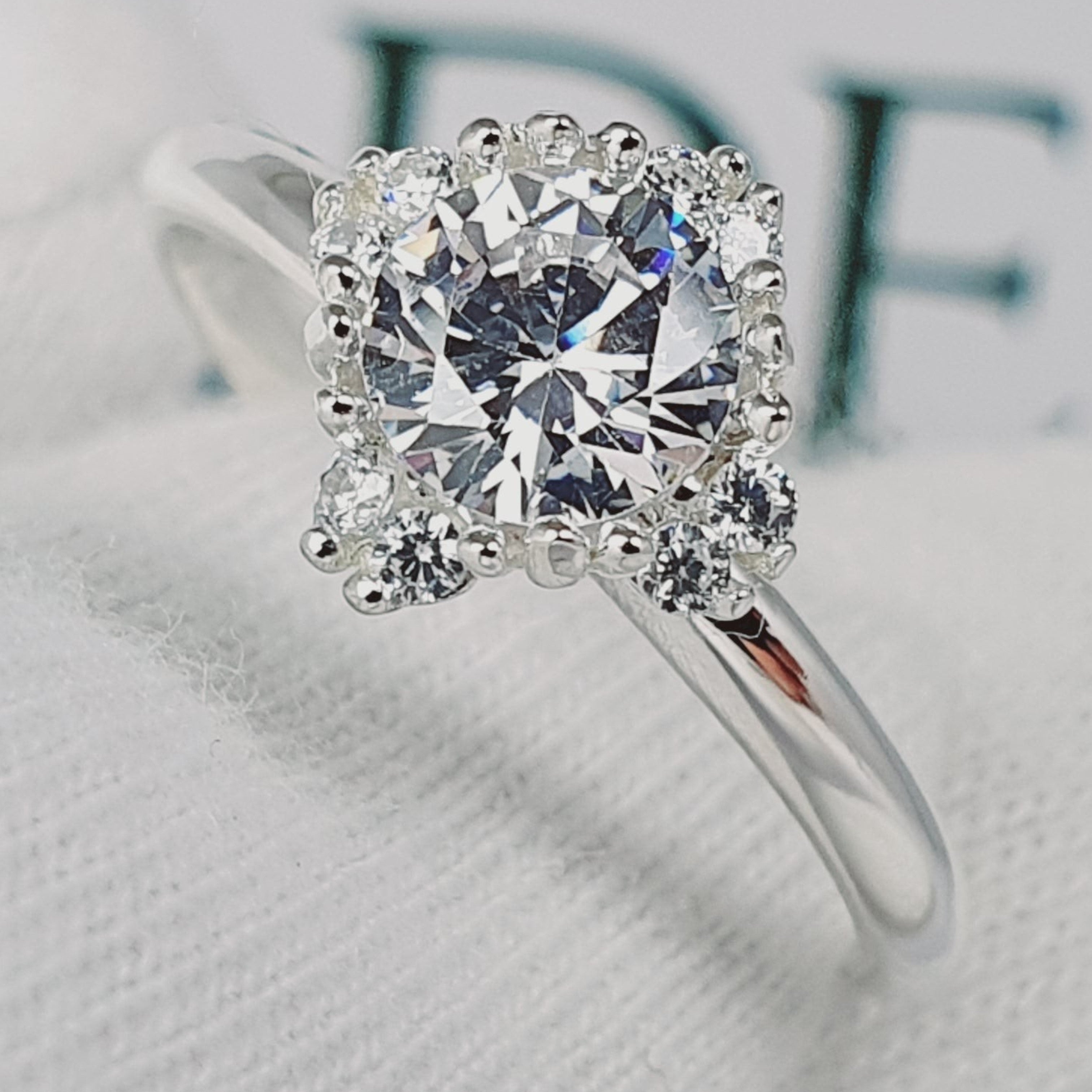 Jade18k Damelia engagement ring with a round-cut center diamond surrounded by smaller stones in a silver band.