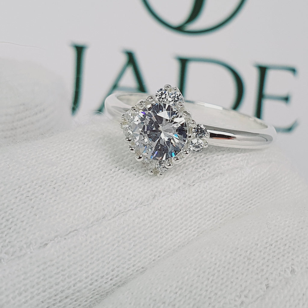 Jade18k Damelia engagement ring in silver with a central round-cut diamond surrounded by smaller stones in a floral halo setting.
