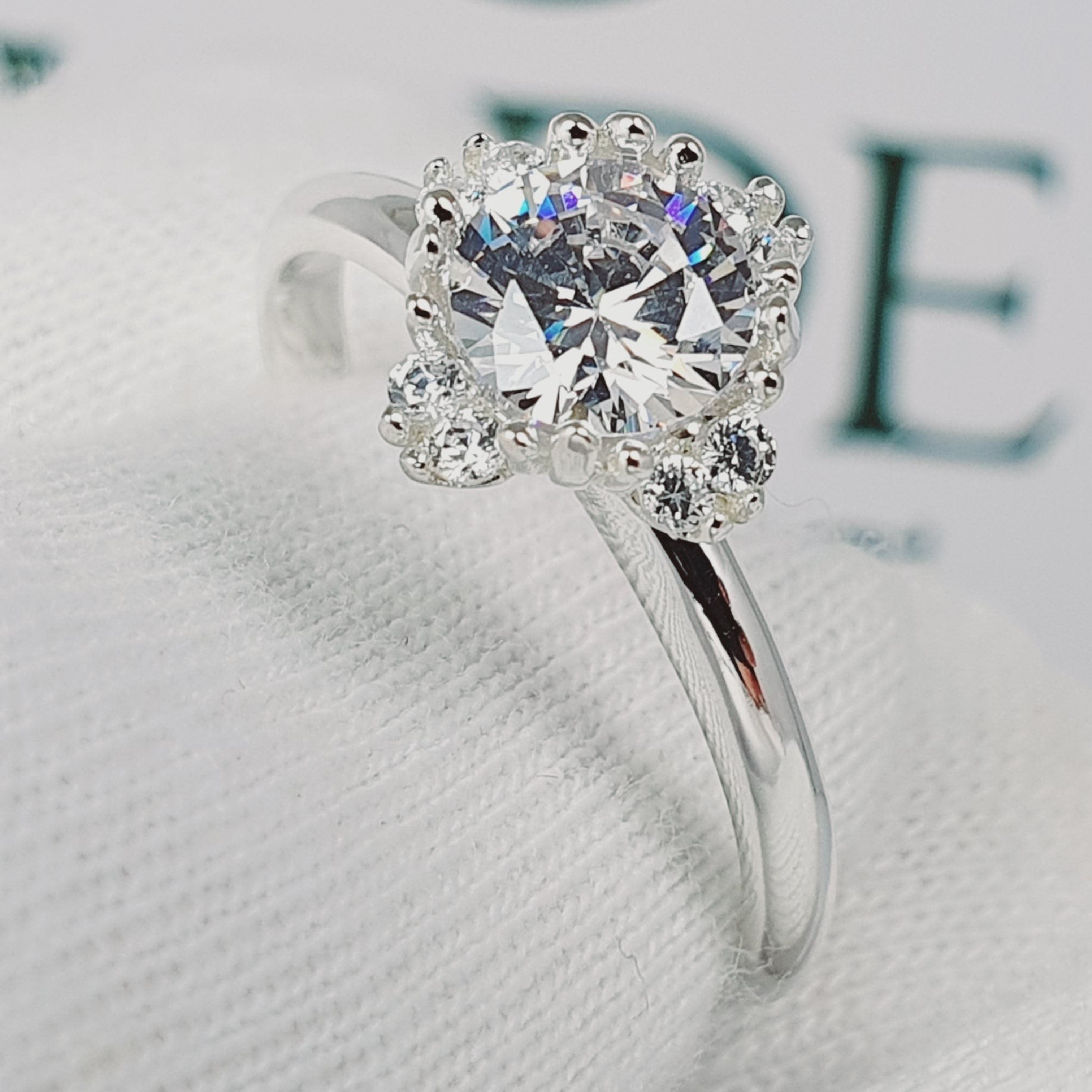 Jade18k Damelia engagement ring in silver with a large central diamond surrounded by smaller stones and a beaded halo.