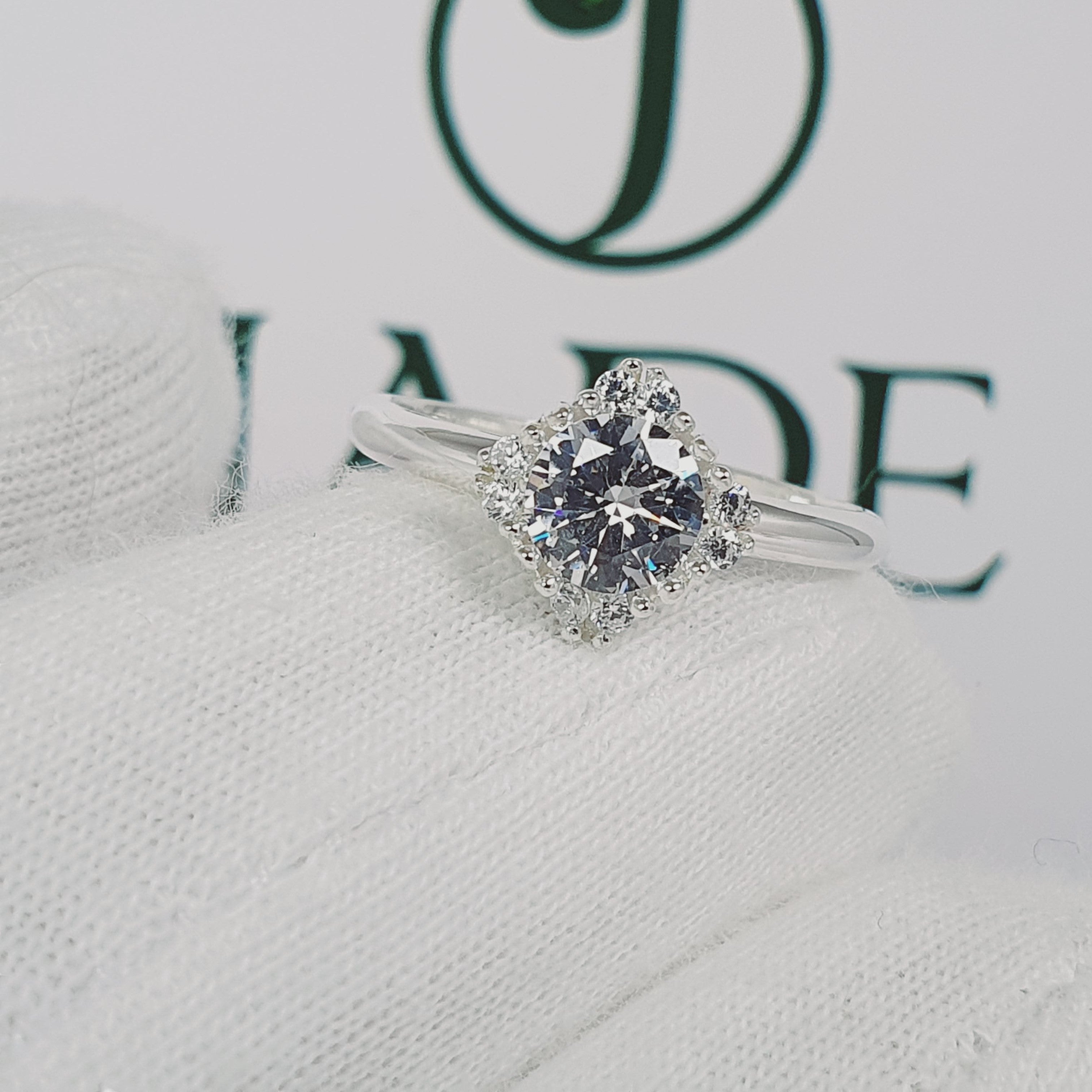 Jade18k Damelia engagement ring in silver with a central round-cut diamond surrounded by a halo of smaller diamonds.