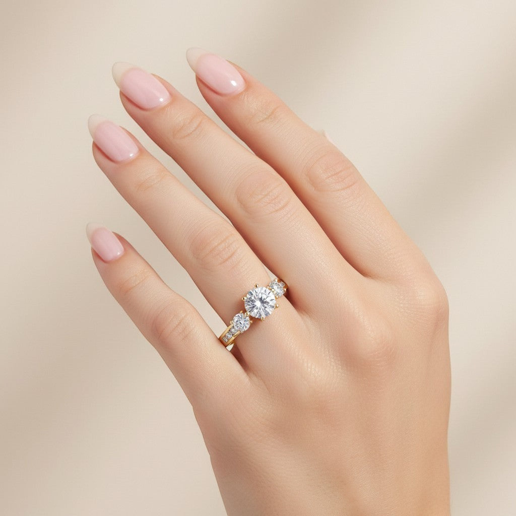 Jade18k yellow gold three-stone engagement ring with round and baguette stones on a hand with neutral polish.