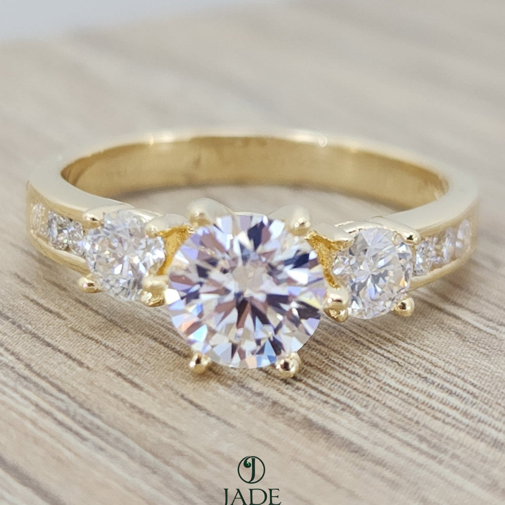 Jade18k yellow gold three-stone engagement ring with a round-cut center stone and channel-set accent stones.
