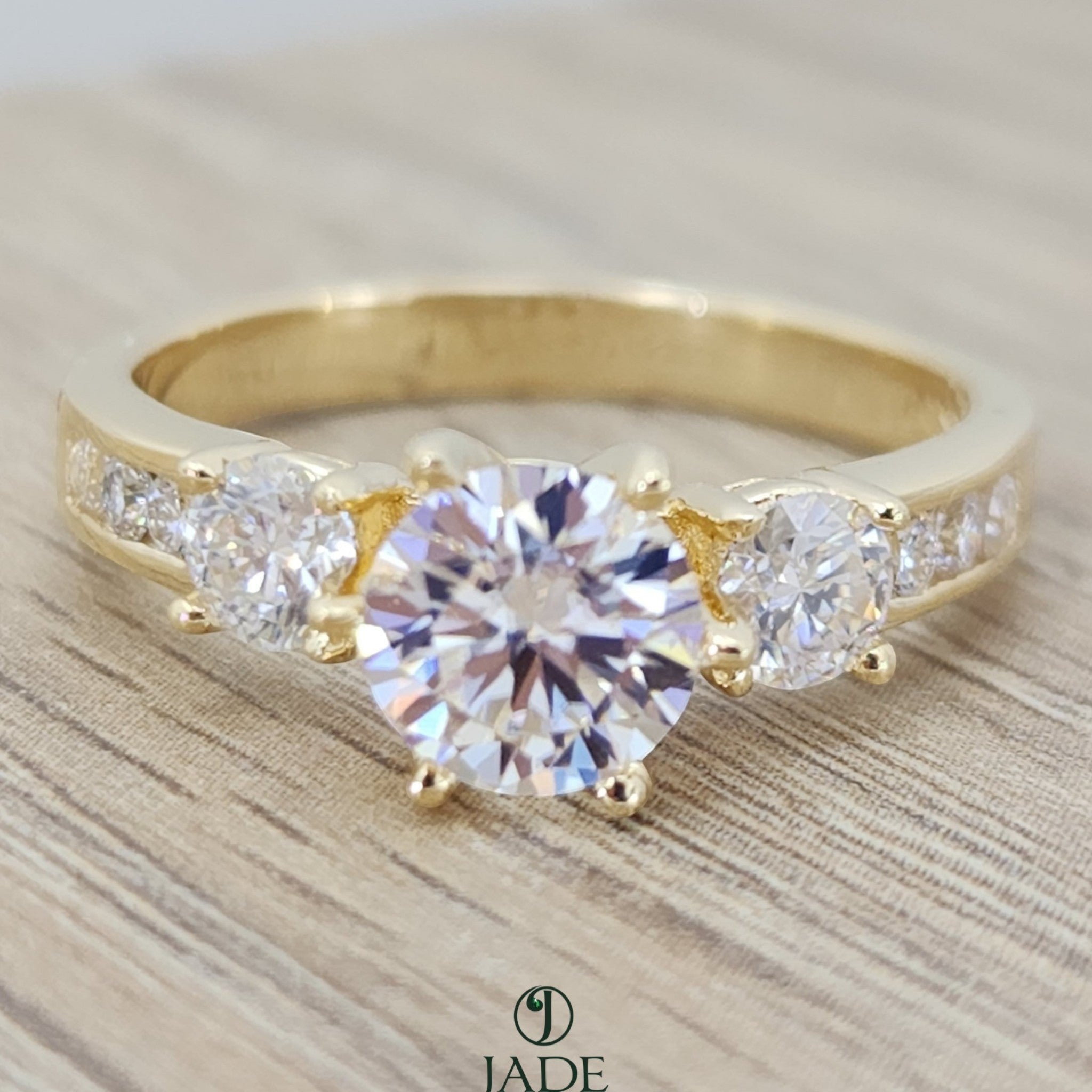 Jade18k yellow gold three-stone engagement ring with a round-cut center stone and channel-set accent stones.