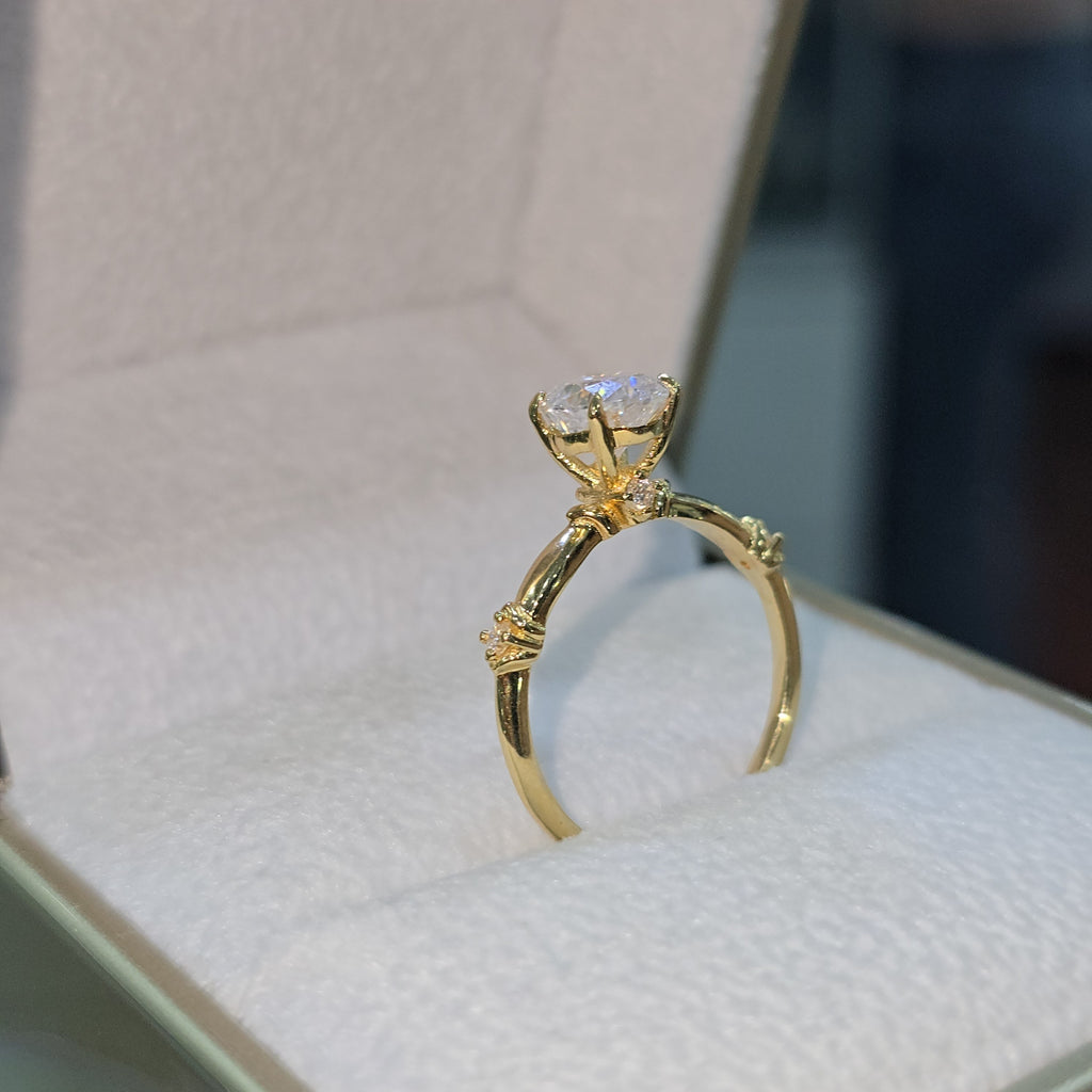 Jade18k 18k yellow gold engagement ring with a round moissanite center stone and small accent stones on the band.