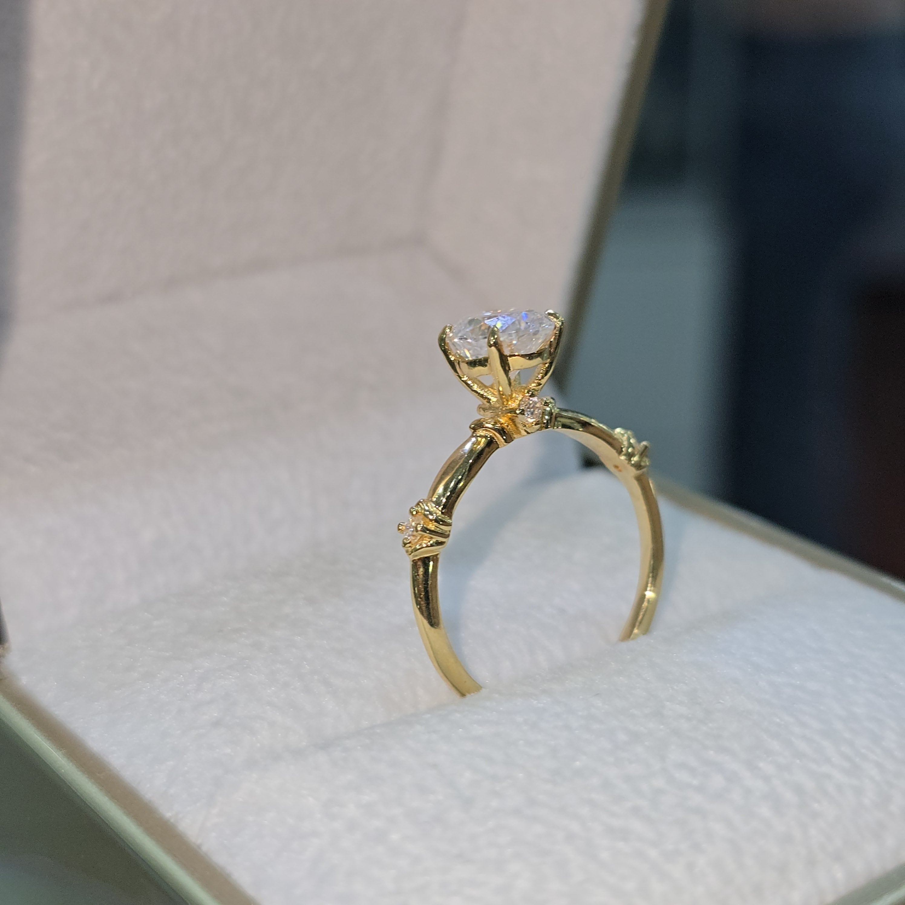 Jade18k 18k yellow gold engagement ring with a round moissanite center stone and small accent stones on the band.