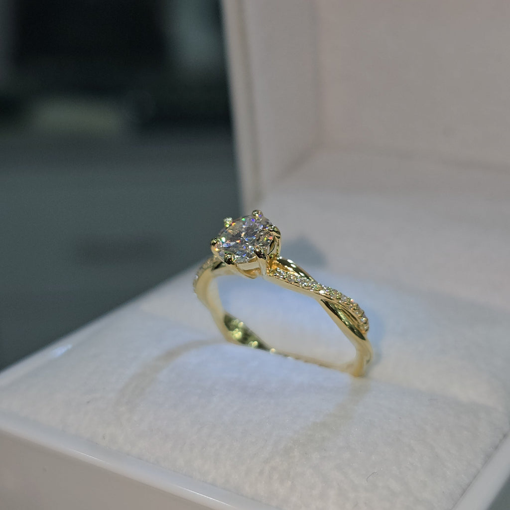 Jade18k 18k yellow gold engagement ring with a central moissanite stone and a twisted band with small diamonds.
