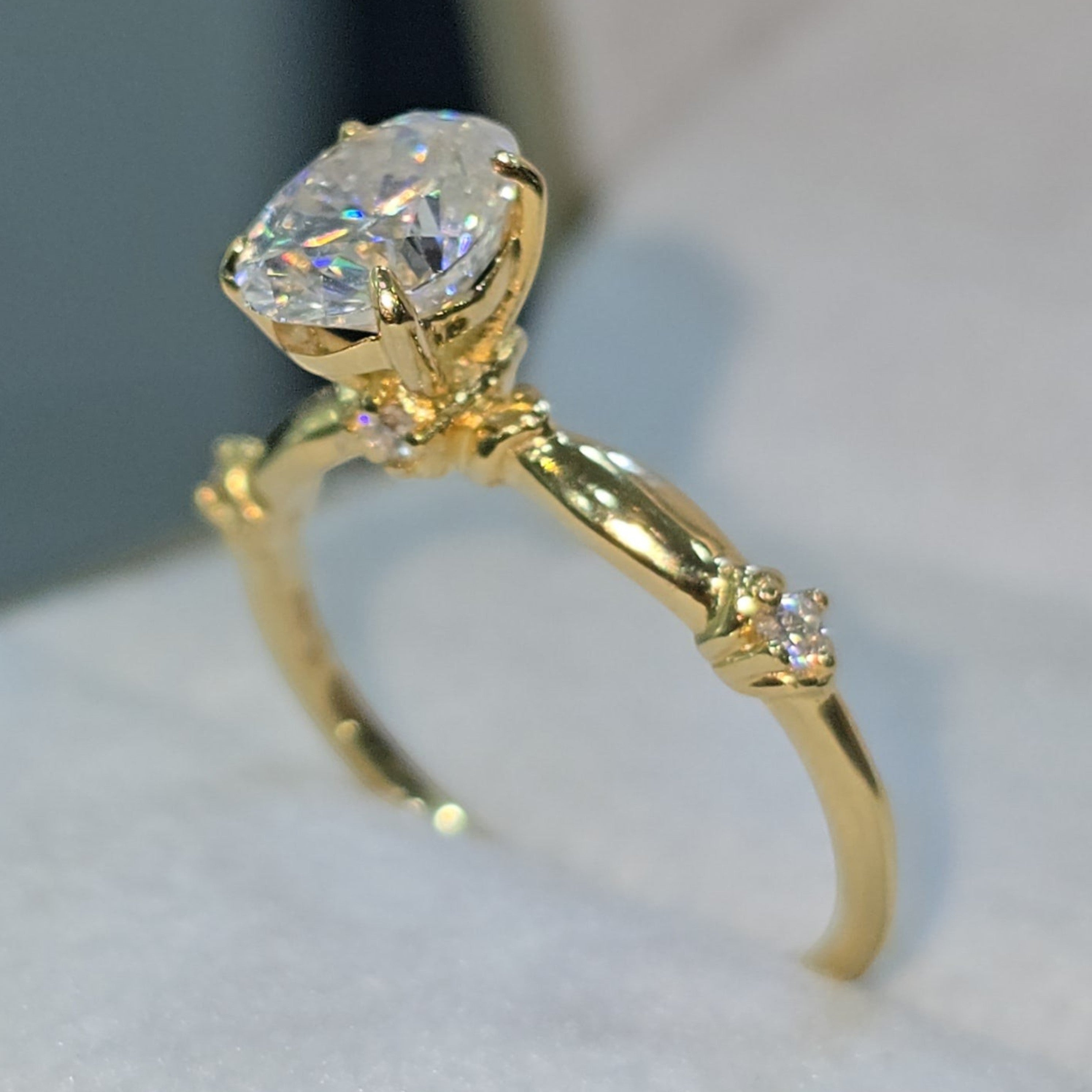 Jade18k 18k yellow gold engagement ring with a large oval moissanite center stone and small accent stones on the band.