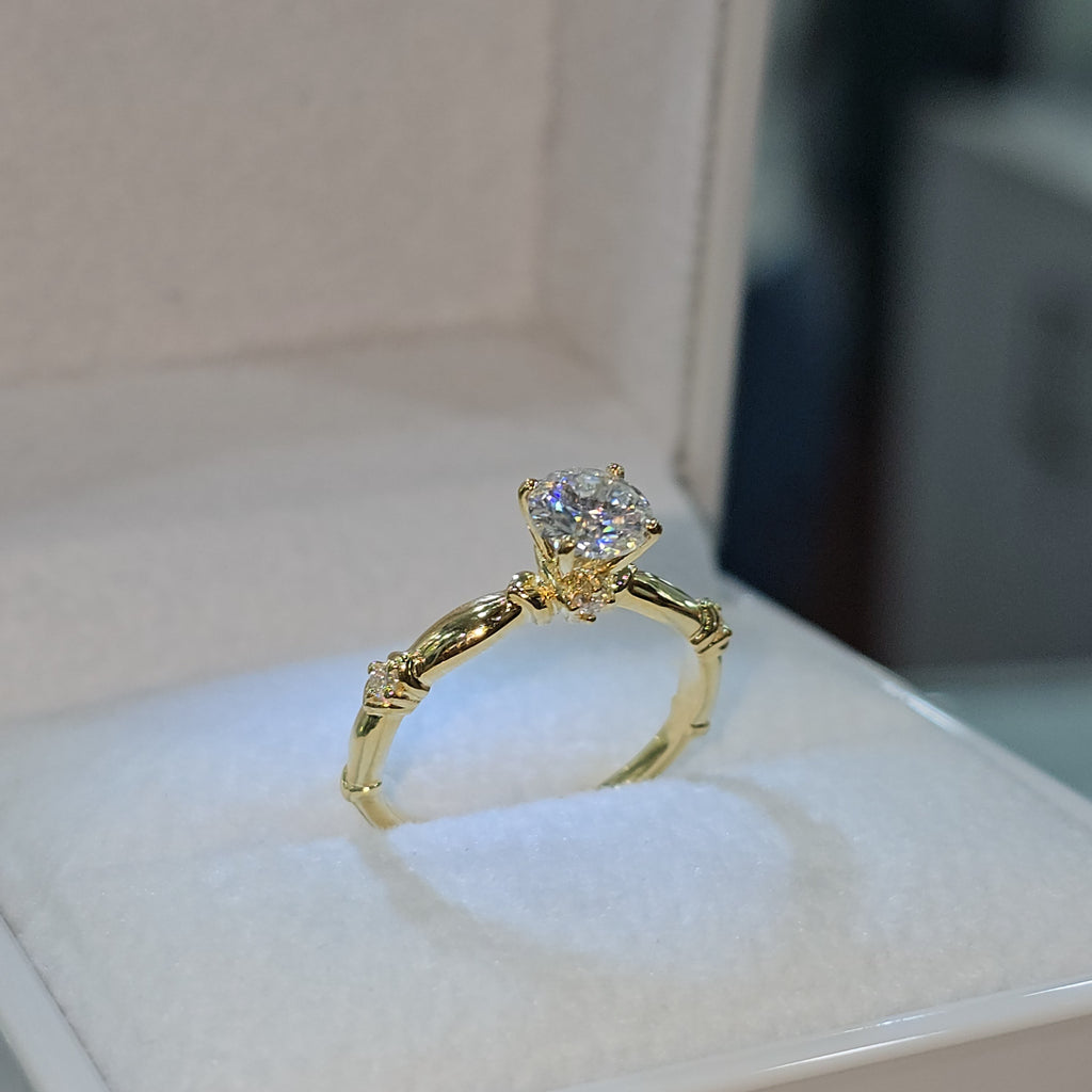 Jade18k 18K yellow gold engagement ring with a round brilliant moissanite center stone and small accent stones on the band.