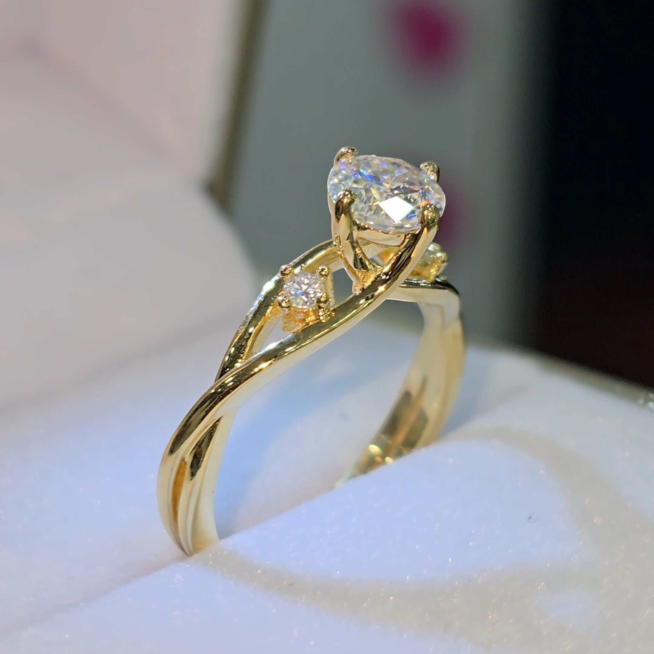 Jade18k yellow gold engagement ring with a pear-cut moissanite center stone and two small accent stones on a twisted band.
