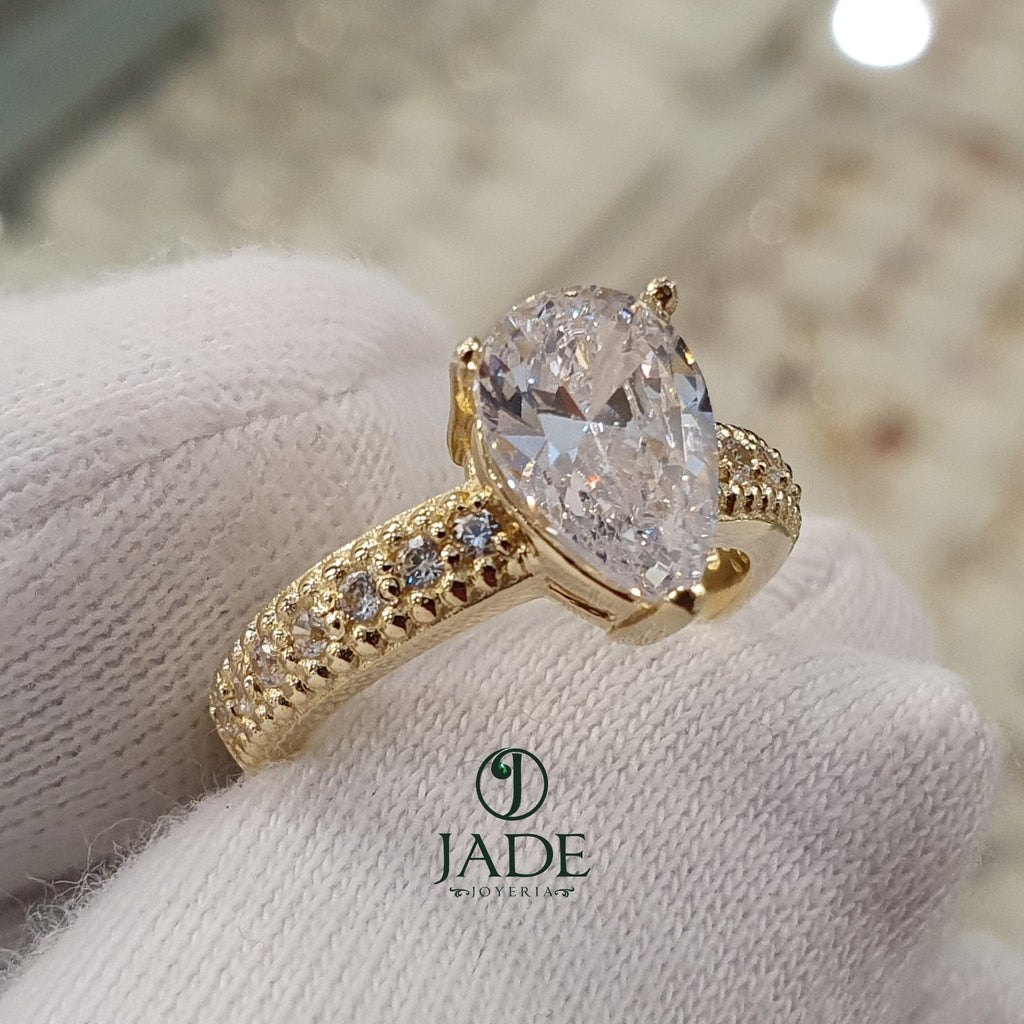 Jade18k 18k yellow gold engagement ring with a pear-cut cubic zirconia and pave set stones on the band.